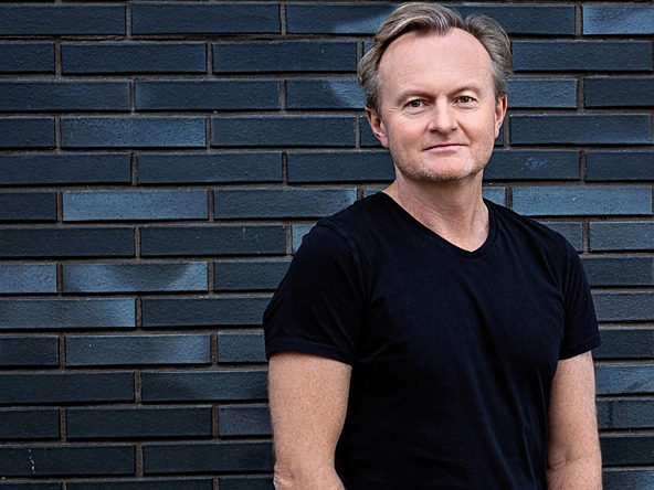  Duncan Grierson standing infront of a blue brick wall